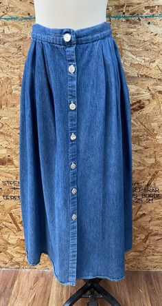 "This is a great vintage button down denim skirt, circa 1980s. It has full skirt styling with pleats and two pockets. Made in USA. 100% cotton. It is in overall good vintage condition. The only flaw noted is that the right side of the skirt seems a little faded. Labeled a vintage size 8, but Most likely would fit a modern size XS/ S. Please check measurements and condition notes below: Waist: 12.5\"-14\" Overall total length: 36\" Please ask questions through Etsy messages. Since this is a vinta Dark Wash Button-up Cotton Skirt, Cotton Skirt With Buttons In Medium Wash, Button-up Denim Blue Cotton Skirt, Denim Blue Button-up Cotton Skirt, Button-up Cotton Denim Skirt With Pockets, Vintage Medium Wash Skirt With Pockets, Medium Wash Button-up Cotton Skirt, Vintage Buttoned Denim Skirt For Spring, Vintage Denim Skirt With Button Closure