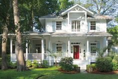 a large white house with red door and windows in the front yard, surrounded by trees