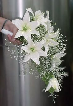 a bouquet of white lilies is being held by someone's hand in front of a refrigerator