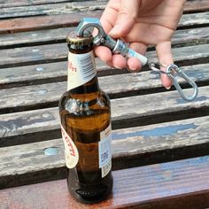 a person holding a beer bottle with a corkscrew in front of it on a wooden bench