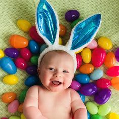 a baby wearing bunny ears laying on top of colorful candy candies in the shape of an egg