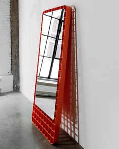 a red mirror sitting on top of a wooden shelf next to a window in a white room