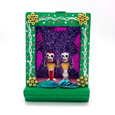 two little skeletons are standing in front of a green frame with purple and yellow decorations