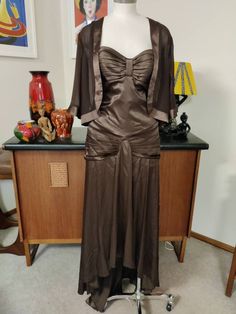 This is the dress to wear to stand out in a crowd by Mr K label in a brown poly satin with a 1930s vibe, very old Hollywood. The dress is a bit big for the size 10au mannequin ( it is a size 12) Has spaghetti straps, a pleated bra section then fitted to a hip swag with a material fold to the below knee length, then dipping through the sides and to a floor length at the back. The back has as a very low dipped back with the pleating at the hips continued from the front. Securing the dress is a str Brown Satin Party Dress, Brown Fitted Evening Dress, Formal Brown Lined Dress, Brown Vintage Evening Dress, Vintage Brown Evening Dress, Elegant Brown Lined Dress For Evening, Elegant Brown Lined Evening Dress, Old Hollywood Style, Hollywood Style