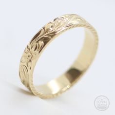 a gold wedding ring with an intricate design on the inside and outside, sitting on a white surface