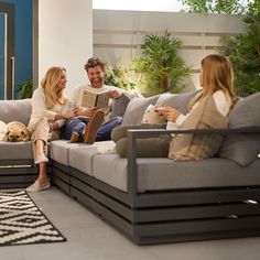 a man and woman sitting on a couch with a dog in front of them reading a book