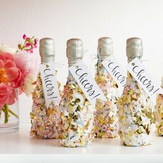 four bottles with labels on them are sitting next to a vase filled with pink flowers