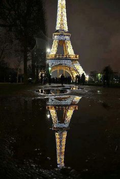 the eiffel tower is lit up at night with its reflection in the water