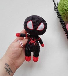 a hand holding a small crocheted spider man doll next to some yarn balls