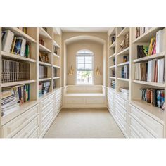 a long white book shelf filled with lots of books next to a window in a room