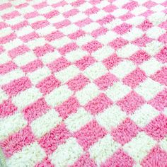 a pink and white crocheted blanket laying on top of a bed