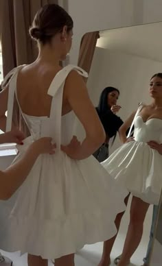 a woman in a white dress looking at herself in the mirror while another person takes a photo