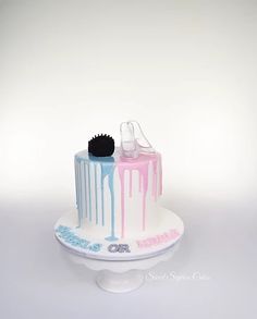 a white cake with pink and blue drips on it sitting on a table next to a black brush