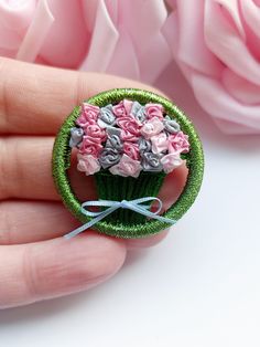 a hand holding a miniature cupcake with pink roses in the background and green ribbon around it