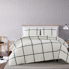 a bed with white and black comforter in front of a brick wall next to a chair