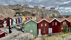 many small houses are painted red, green and blue in front of a rocky cliff