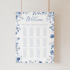 a blue and white floral wedding seating chart hanging from a string on a wall,