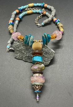 "Bohemian Longer gem necklace with a wired and beaded Pendant.  I just love colors, shapes, and different sizes in materials.  You will see apatite stone, lavender amethyst, vintage glass, wood, brass, copper, wood, lamp work beads hand crafted from Thailand and glass tube beads from Africa, in this unique necklace.  I wired the pendant and stacked up the beads.  I crafted the curved portion of this necklace and beaded onto wire; this helps to hold the curved shape.  Then I beaded strands from t Bohemian Purple Beaded Necklaces With Czech Glass, Bohemian Adjustable Beaded Stone Necklaces, Beaded Bohemian Czech Glass Crystal Necklace, Bohemian Beaded Czech Glass Crystal Necklaces, Bohemian Beaded Czech Glass Crystal Necklace, Bohemian Beaded Gemstone Dangle Necklace, Bohemian Beaded Gemstone Dangle Necklaces, Bohemian Dangle Gemstone Beaded Necklaces, Bohemian Gemstone Beaded Dangle Necklaces