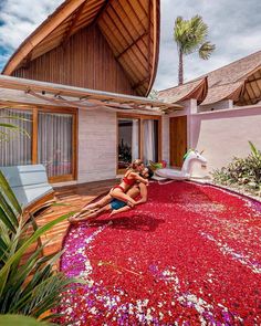 a woman sitting on top of a red rug next to a pool covered in flowers