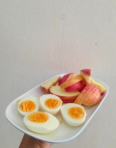 someone is holding a plate with hard boiled eggs and sliced apples on it in front of a white wall