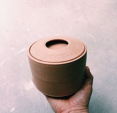 a hand is holding a clay pot with a lid