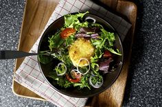 a salad in a black bowl on top of a wooden cutting board next to a knife