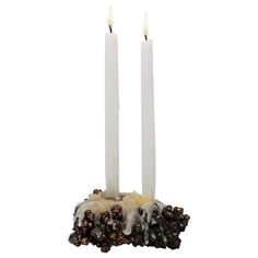 two white candles are sitting on top of some black and white rocks with sprinkles