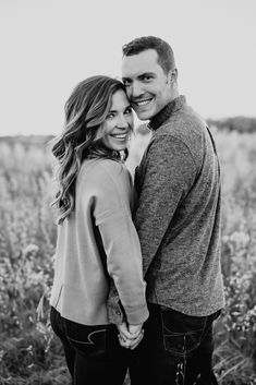 black and white photo of couple holding hands in field with wildflowers behind them