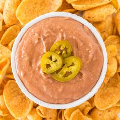 a white bowl filled with chips and topped with a red dip surrounded by sliced jalapenos