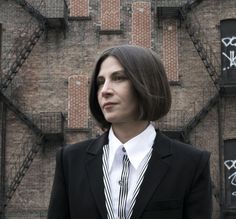 a woman standing in front of a brick building with graffiti on it's walls