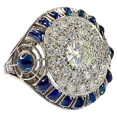 This Art Deco-style ring is crafted in platinum 950 and features Sapphires and Diamonds. It has a weight of 7.5 grams and is sized 16/56. The Diamonds are brilliant-cut, with a central stone of 0.50 carats and a total weight of 1.22 carats. They are of VS-SI clarity and G-H color grade. The Sapphires are cabochon-cut and other custom cuts to fit the piece. The gemstones are set in a grain setting, and the front motif measures 2 cm x 2 cm. ** IN STOCK** Characteristics: Material: Platinum 950 Central Diamond: 0.50 ct, Brilliant Cut Total Diamonds: 1.22 ct total, Brilliant Cut, VS-SI Clarity, G-H Color Sapphires: Cabochon and Custom Cuts Weight: 7.5 grams Ring Size: 16/56 Setting: Grain Front Motif Dimensions: 2 cm x 2 cm Art Deco Drop Earrings, Vintage Cluster Ring, Art Deco Diamond Rings, Blue Sapphire Diamond, Gold Art Deco, Art Deco Diamond, Gold Art, Art Deco Ring, Sapphire Engagement