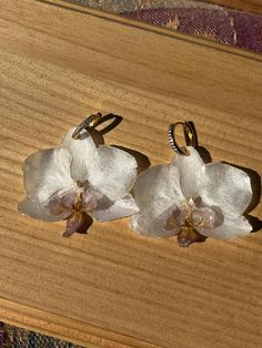 White orchid earrings handmade using real flowers! The flowers are harvested, dried for a week+, coated in resin and put on an earring.  🔅🔆Hoops can be swapped out for a different metal/ size/ shape as long as I have it in stock. Message me if you have any requests! 🔆🔅 ** Product shape and color may vary slightly from photographs **  Do not submerge in water All flowers are unique and one of a kind. No two flowers are perfectly identical. Some may have imperfect edges, slightly different shapes, or coloring. All flowers are listed on Etsy in the state you will receive them. Thoroughly looking through the photos and video before purchasing will ensure you know exactly what you are receiving!  Thank you! Resin Orchid Earrings, Handmade Orchid Earrings, White Pressed Flowers Earrings, White Pressed Flower Earrings For Wedding, White Flower Earrings With Pressed Flowers For Wedding, White Earrings With Pressed Flowers, White Flower Resin Earrings, White Resin Earrings With Pressed Flowers, Elegant White Earrings With Pressed Flowers