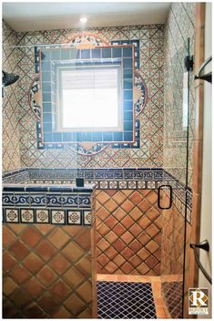 a tiled bathroom with blue and brown tiles on the walls, shower stall and window