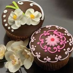 two decorated cupcakes sitting next to each other on top of a table with flowers