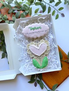 an open box with some cookies in it on a table next to leaves and flowers