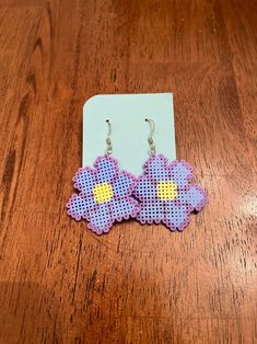 a pair of purple and yellow flower shaped earrings sitting on top of a wooden table