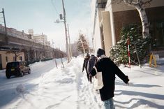 several people walking down a snowy street with snowboards on their backs and one person carrying a snowboard