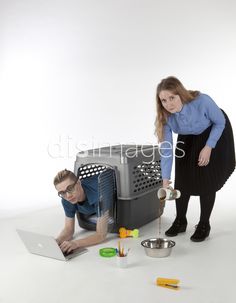 two people standing over a cat in a cage and looking at a laptop computer on the floor