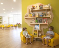 two children sitting on yellow chairs in a room with bookshelves and wooden floors