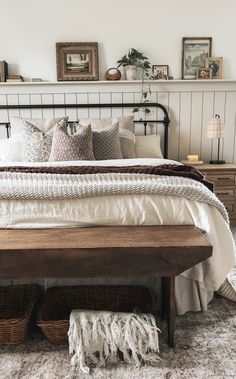 a bed with pillows, blankets and baskets on the headboard in a room that has white walls