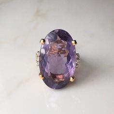 A Vintage 14 carat Gold Amethyst ring framed by diamonds. This beautiful piece displays a gorgeous purple stone in the clutches of a striking gold setting. The shoulders offer a really simple design, but why would it offer anything else, the setting holds so much sparkle and with the stone it's an absolute show stopper! CONDITION: Wear consistent with age and use. Please see photos for more detail. AMETHYST DIAMETER: 25mm x 15mm BAND WIDTH (NARROWEST): 2mm DIAMOND DIAMETER: 1.5mm RING SIZE: UK: P 1/2 | US: 7 3/4 WEIGHT: 12.4 grams (QZZ) Amethyst Cocktail Ring, Gold Amethyst Ring, Gold Diamond Band, Diamond Cocktail Ring, Platinum Diamond Rings, Amethyst Gem, Diamond Cocktail Rings, Purple Band, But Why