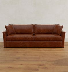 a brown leather couch sitting on top of a wooden floor next to a white wall