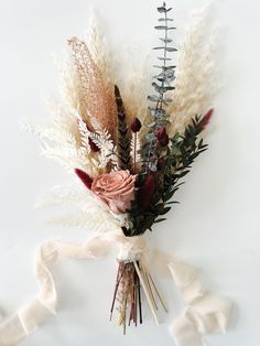 an arrangement of dried flowers and foliage on a white background with ribbon tied around it