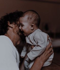 a woman holding a baby up to her face and kissing it's forehead on the cheek