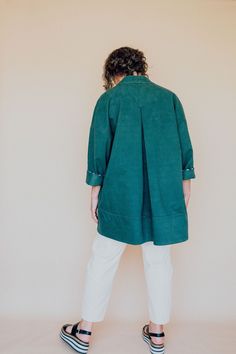 a woman standing in front of a white wall wearing a green coat and striped shoes