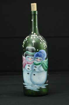 a green bottle with two snowmen painted on the front and sides, sitting on a black surface