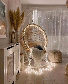 a hanging chair with lights around it in a room that has white curtains and wooden floors