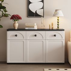 a white cabinet with two vases and candles on top next to a couch in a living room