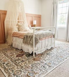 a white bed sitting on top of a rug next to a window