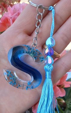 a hand holding a blue glass letter s keychain with tassels and beads